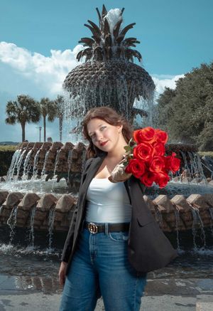 Confident woman holding red roses in front of the Pineapple Fountain in Downtown Charleston, SC.