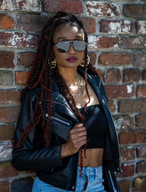 A stylish fashion portrait in Downtown Charleston, SC against a brick wall featuring a black leather jacket and denim outfit combination