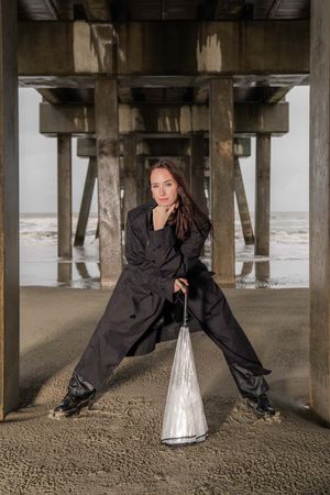 Artistic photos showing a person in black clothing laying on sand beneath a wooden pier at folly beach, sc.
