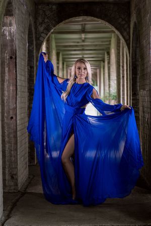 A women poses in flowing royal blue dress poses dramatically in a dark stone corridor with multiple archways in Charleston, SC.