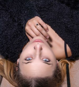 A person lying down with blonde hair and blue eyes gazes upward against a dark background at Pitt Street Bridge in Mount Pleasant, SC.