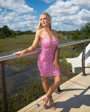 Woman in pink floral dress poses on wooden deck overlooking marsh landscape at Riverfront Park in Charleston, SC.