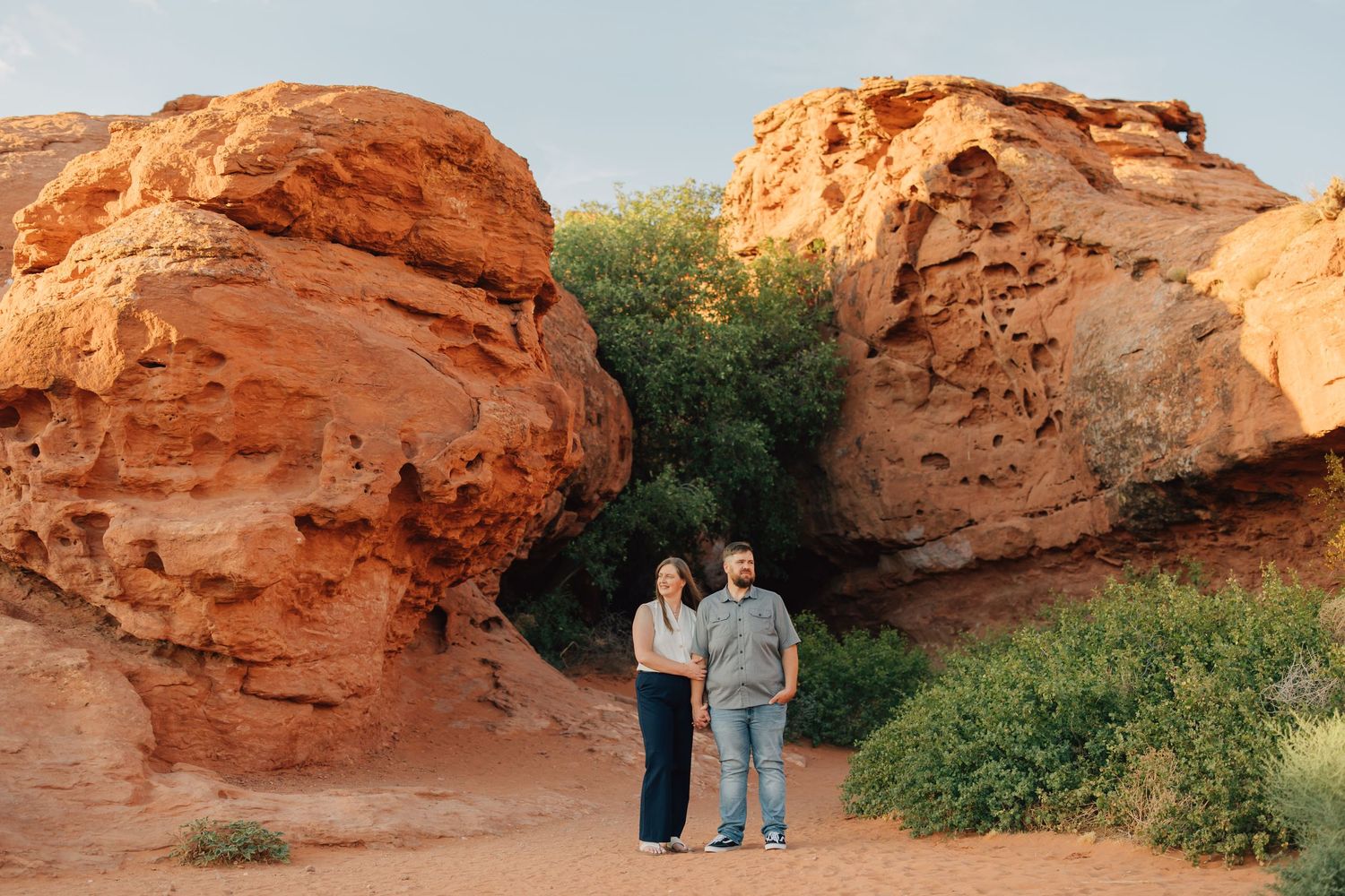 Family embraces and laughs together against stunning red rock formations in desert landscape at sunset.