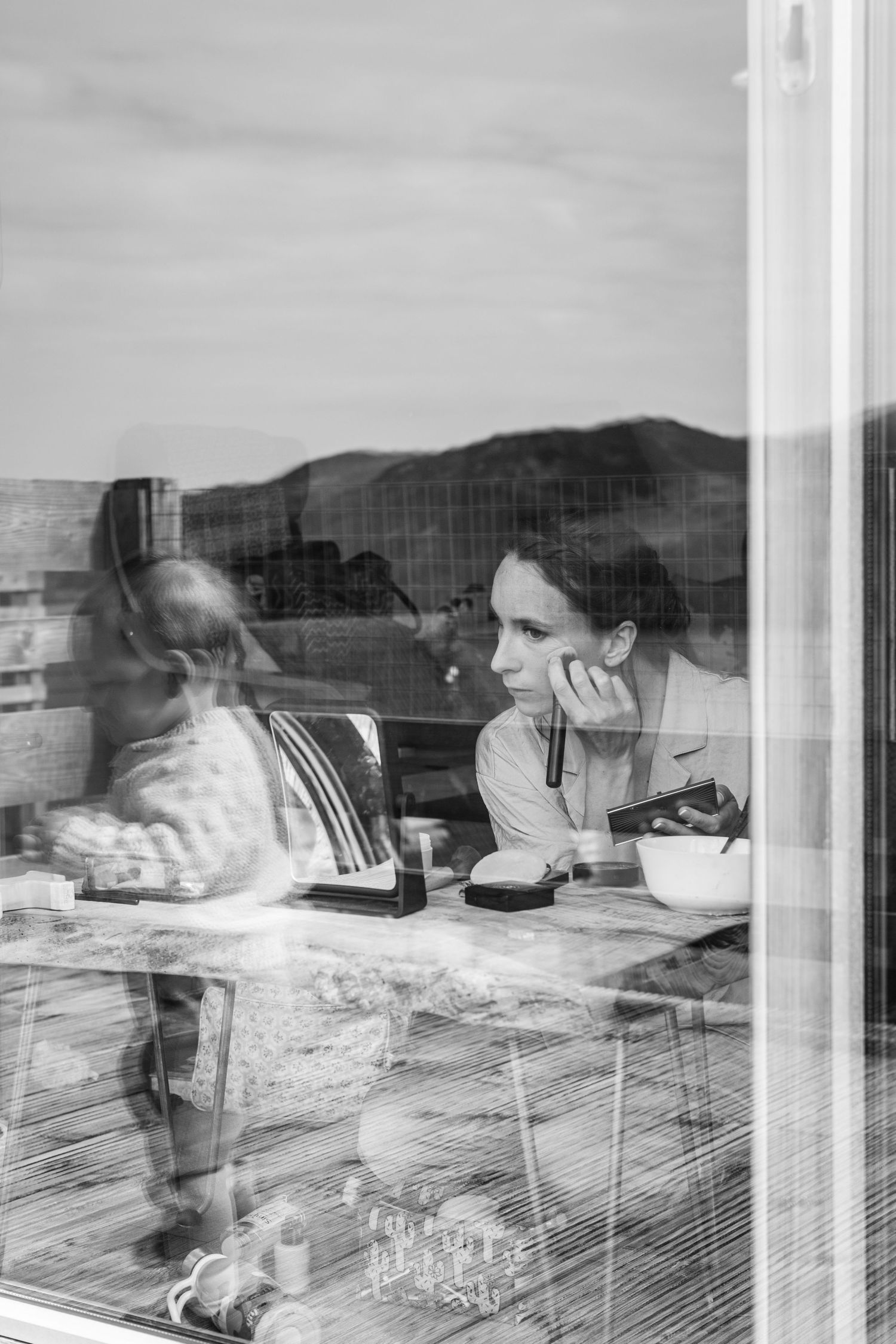 Multiple exposure black and white photograph shows a person working at a desk with mountains visible through windows.