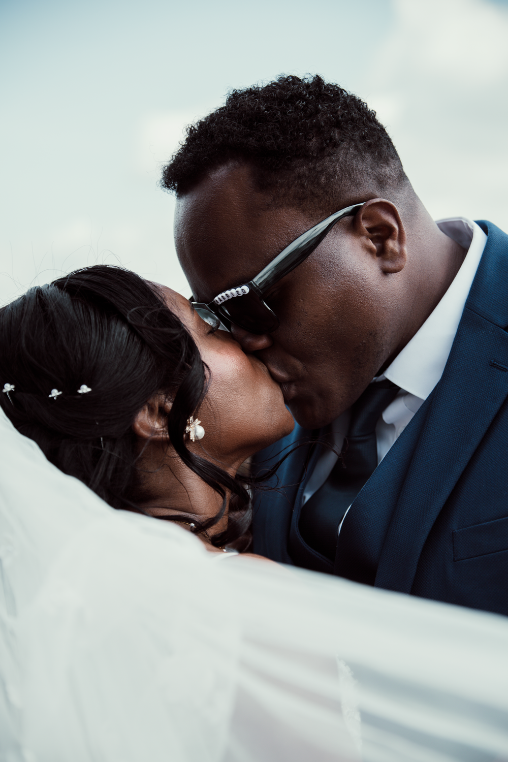 A romantic couple sharing a kiss against a red backdrop with visible tattoo art and elegant attire.