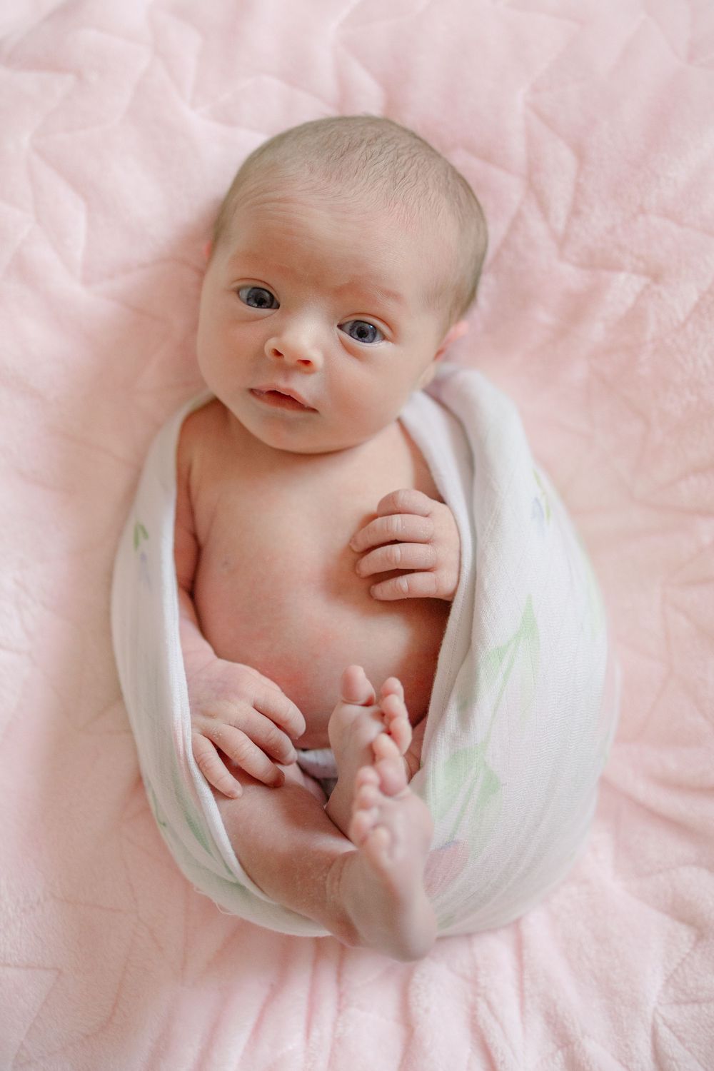 Newborn baby wrapped in soft white fabric against pink background in artistic collage style photography.