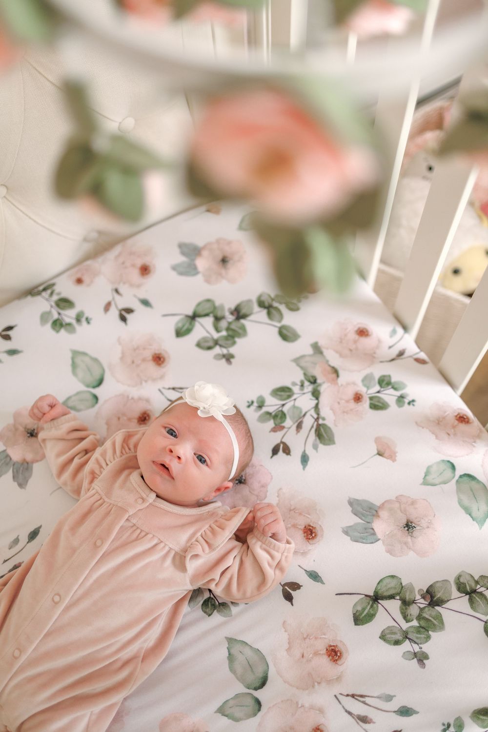 Baby lying on floral bedding with pink roses and green leaves pattern in soft, dreamy lighting.