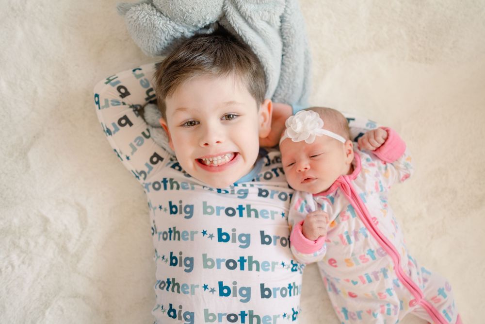 Baby lying on cream colored blanket with 'big brother' text pattern wearing light colored outfit.