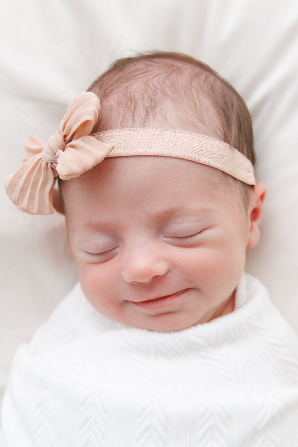 Sleeping newborn wearing a peach bow headband rests peacefully on white bedding in a series of three similar poses.