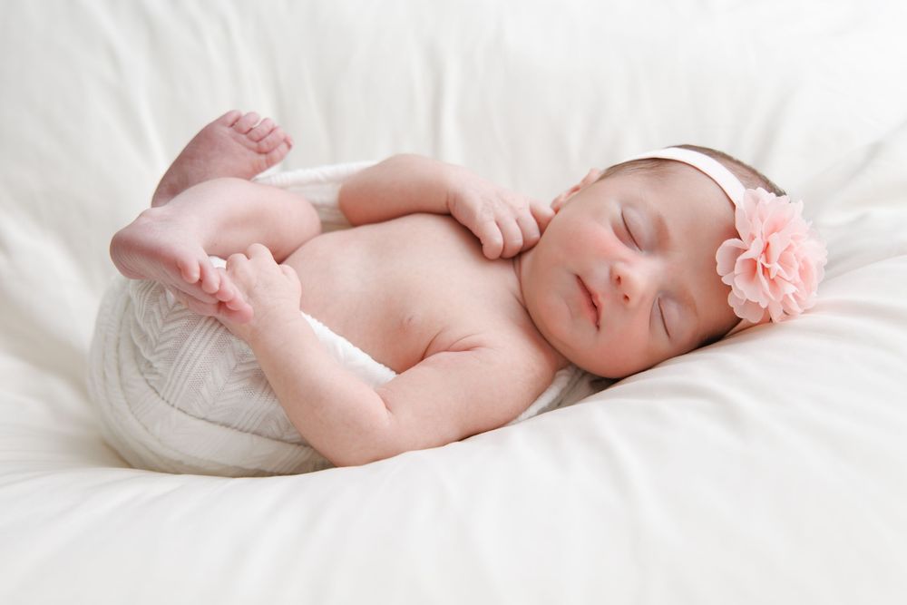 A delicate newborn baby sleeping peacefully on soft white bedding in a minimalist portrait series.