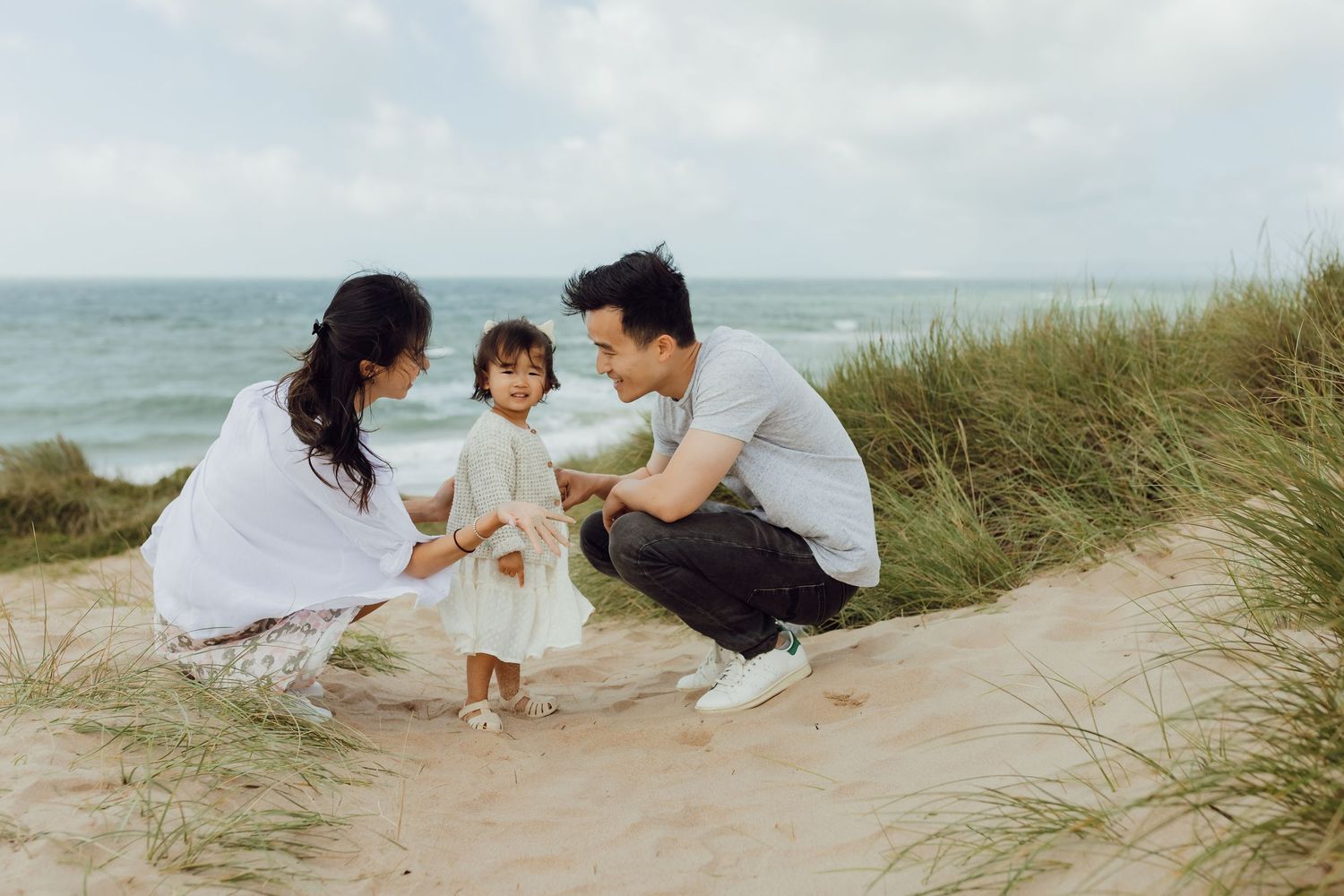 Family of three walking along Dorset beach on a cloudy day, holding their baby close.