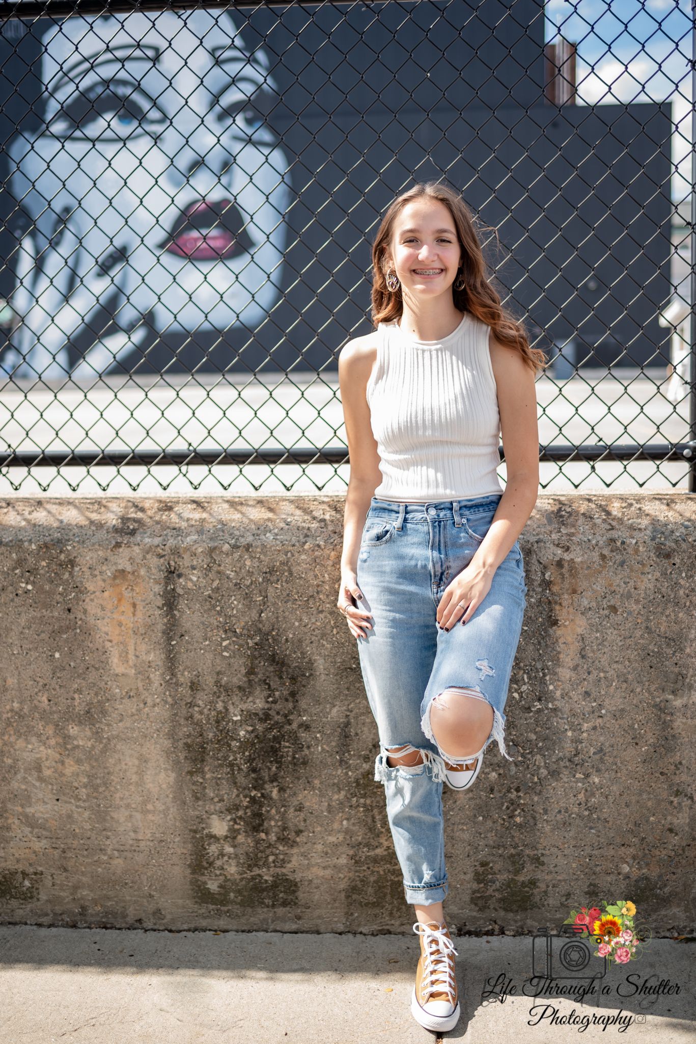 A series of casual outdoor portraits against a concrete wall and chain link fence with sunflowers and ripped jeans.