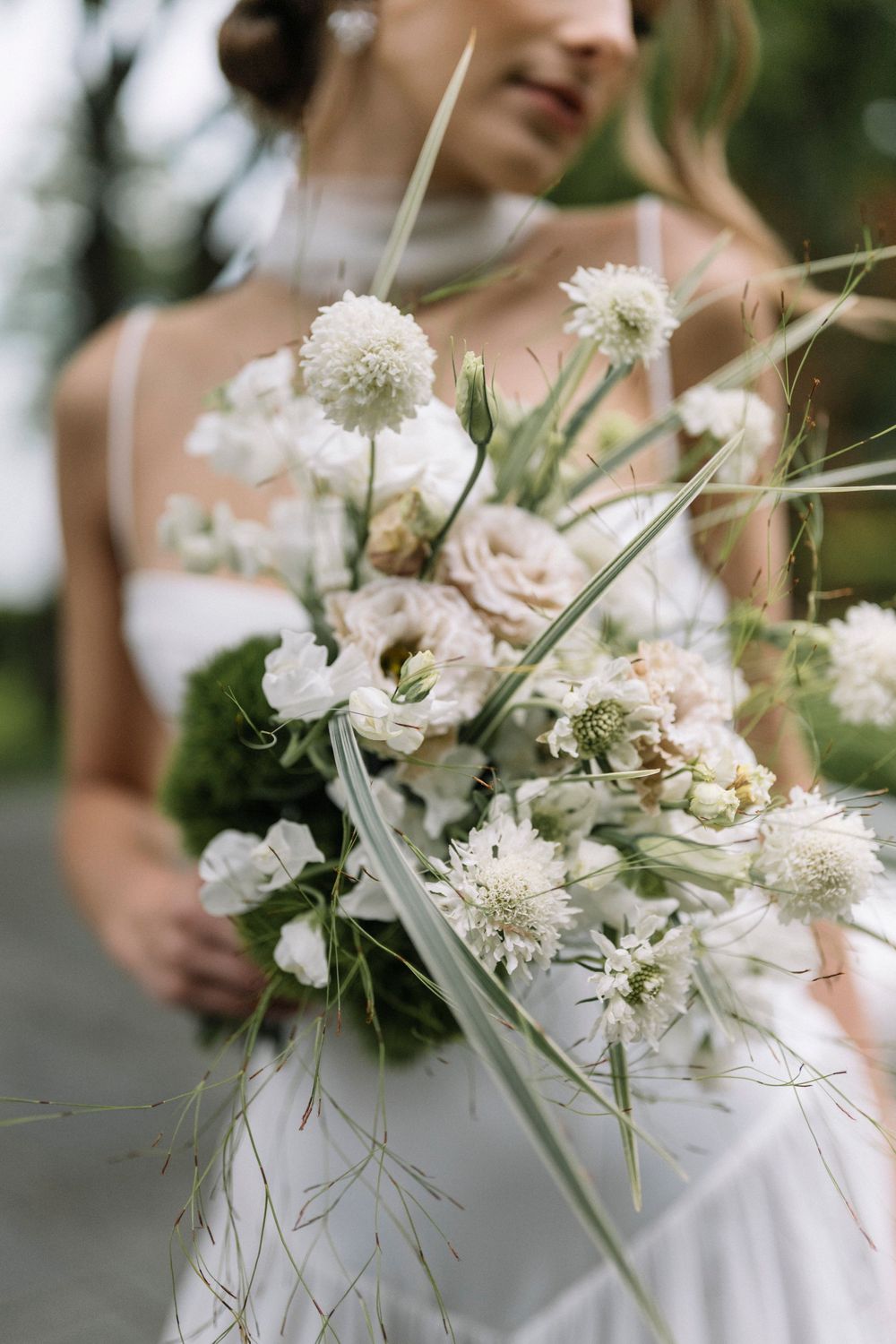 Delicate white floral wedding bouquet with wispy greenery and soft textures captured in natural outdoor lighting.