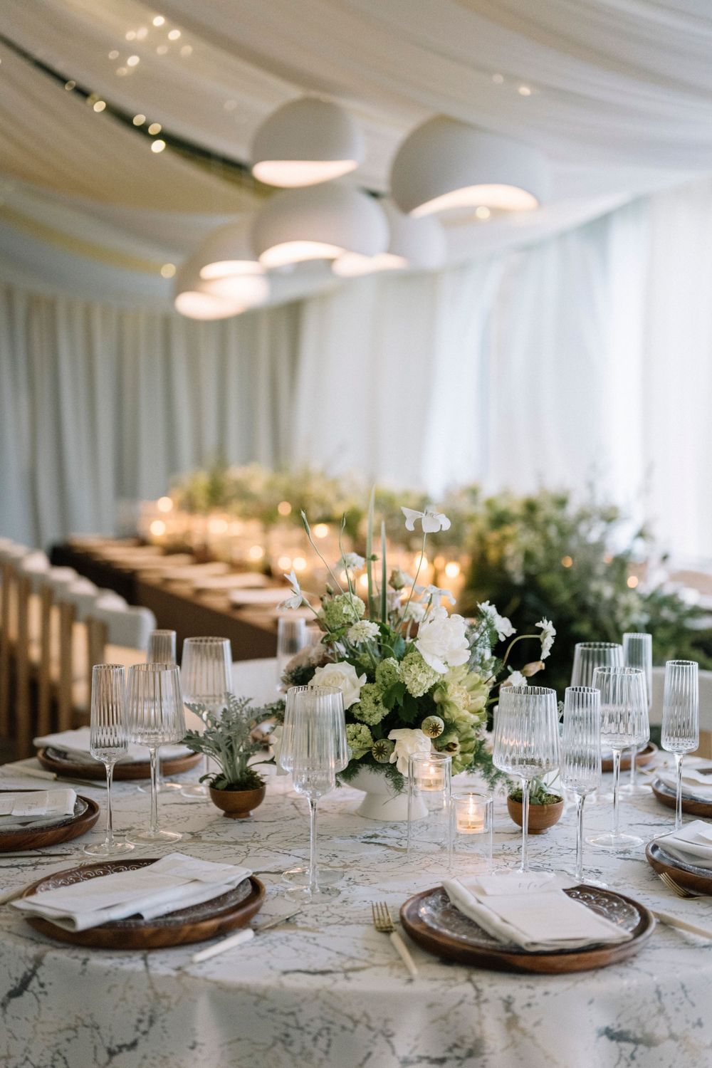 Elegant wedding reception table setting with white floral centerpieces, crystal glassware and draped fabric ceiling decor.