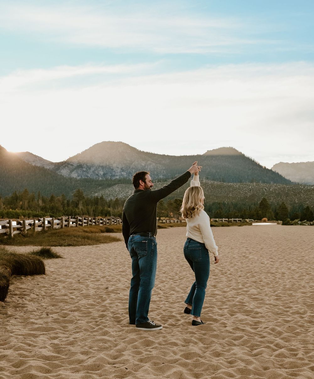 Couple dancing together on a sandy beach with mountains and sunset silhouettes in the background.