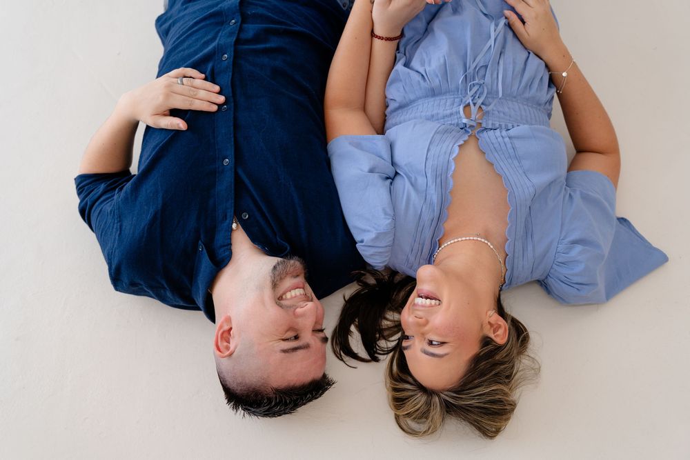 Family lying together on white floor in coordinated blue and gray outfits during lifestyle photoshoot.