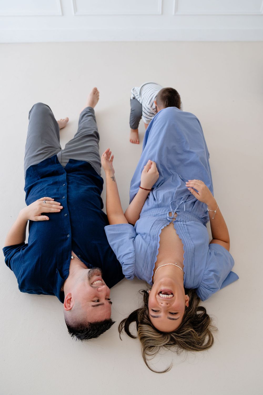 Couple lying on white floor together in casual clothing taking playful photos.