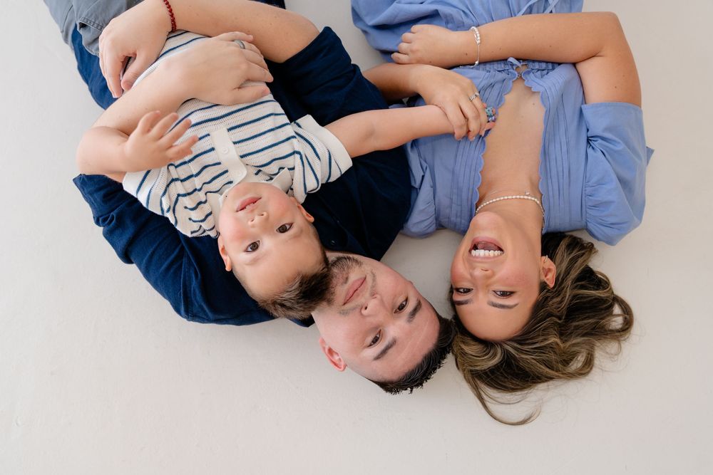 Three people lying on white floor wearing casual clothing while smiling and looking upward together.