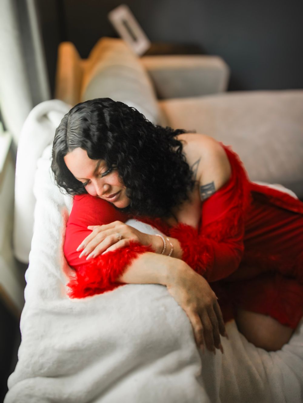 A person in a red dress lies gracefully on a white couch in a series of artistic boudoir photographs.