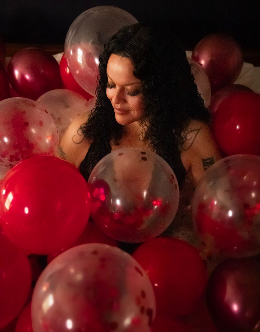 A dreamy portrait surrounded by red and clear balloons in a dark moody setting.