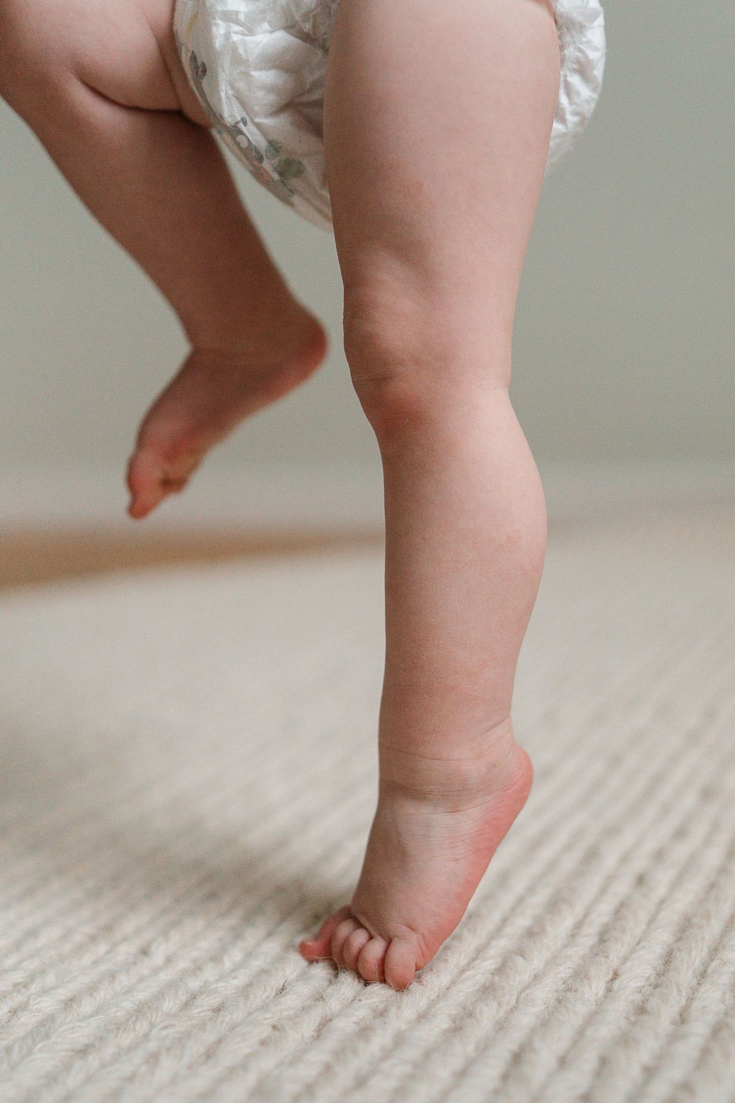 Close-up view of tiny baby feet taking first steps on a beige textured carpet.