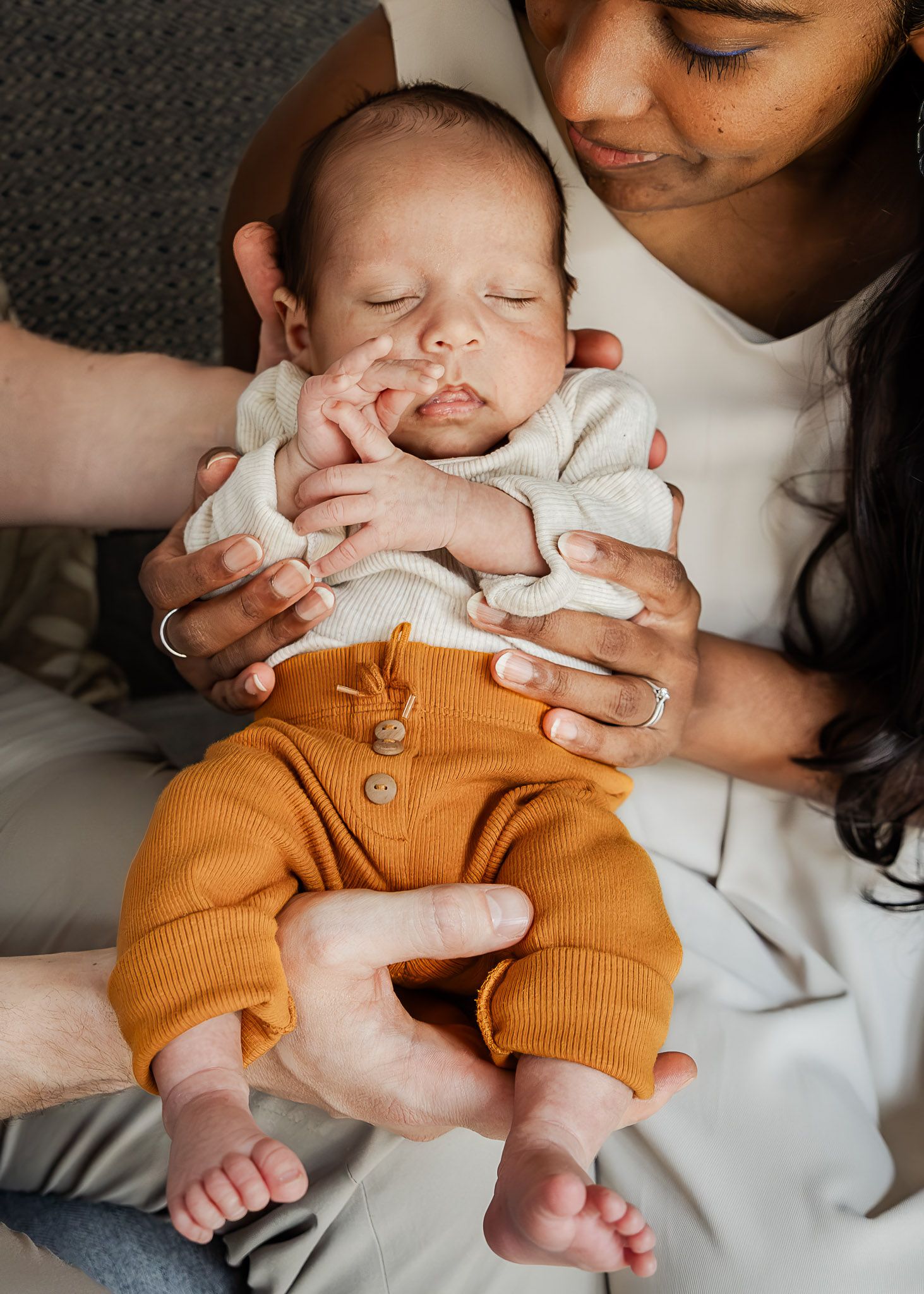 A couple cuddle their small baby on the sofa at home during their relaxed and natural Bristol in home newborn photoshoot