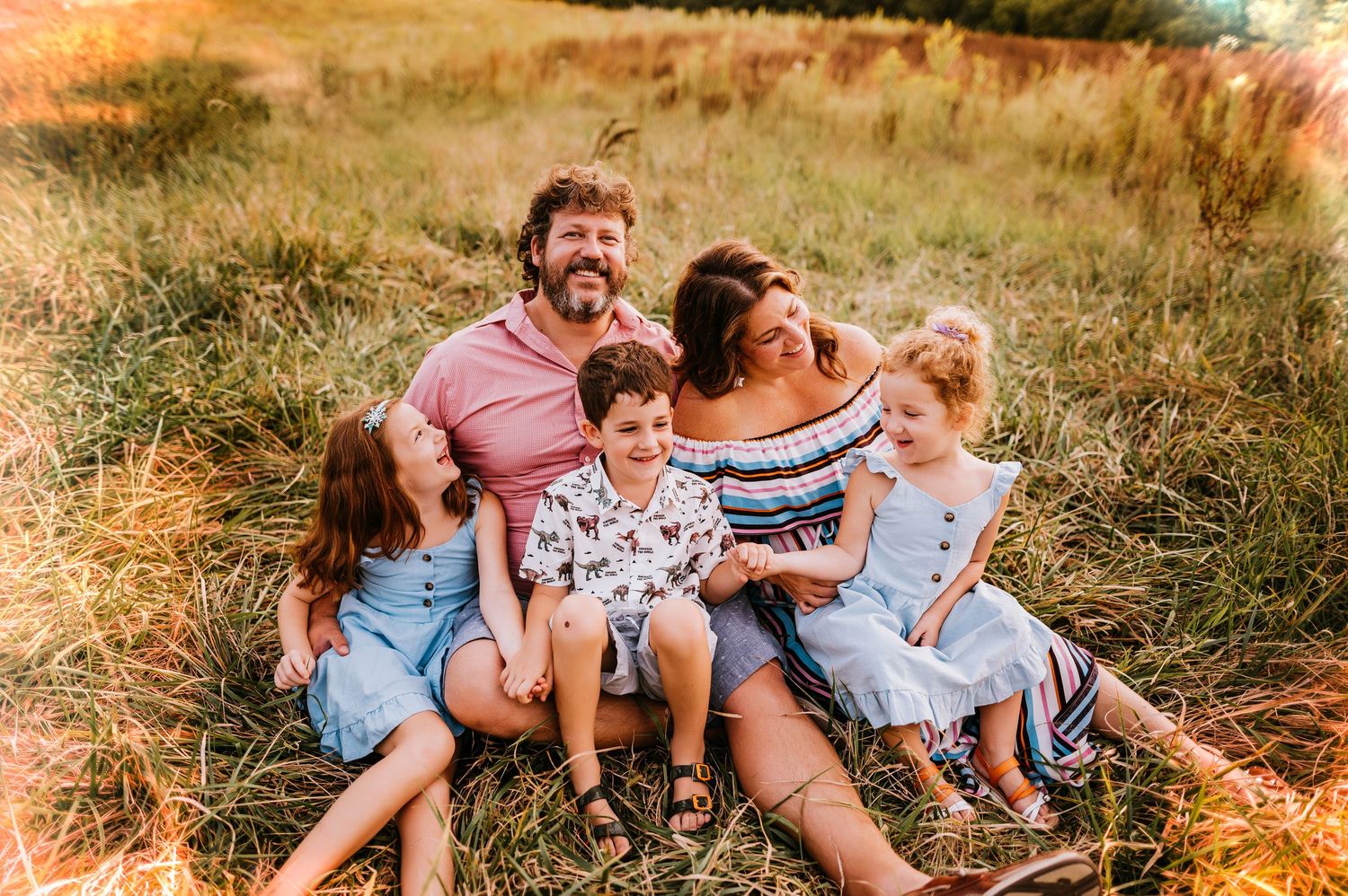 Family sitting together in golden sunlit field during sunset photo session.