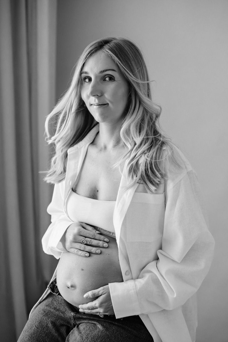 Black and white maternity portrait of an expectant mother in a white shirt and jeans with wavy blonde hair.