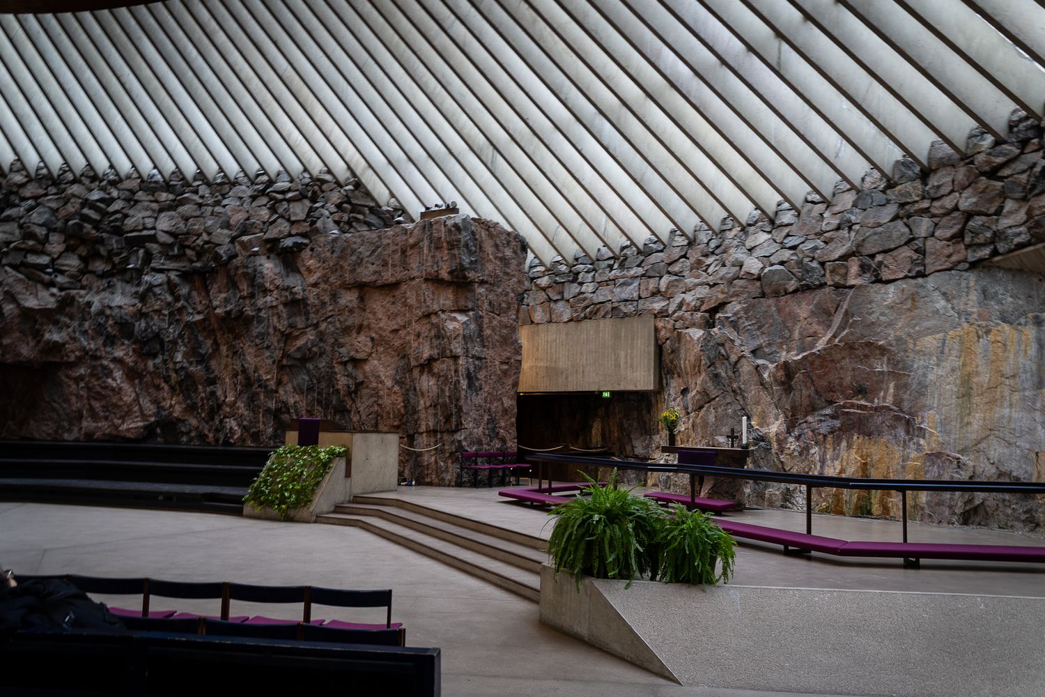 Interior of Temppeliaukio Rock Church Helsinki featuring natural stone walls, wooden ceiling beams, and minimalist altar.
