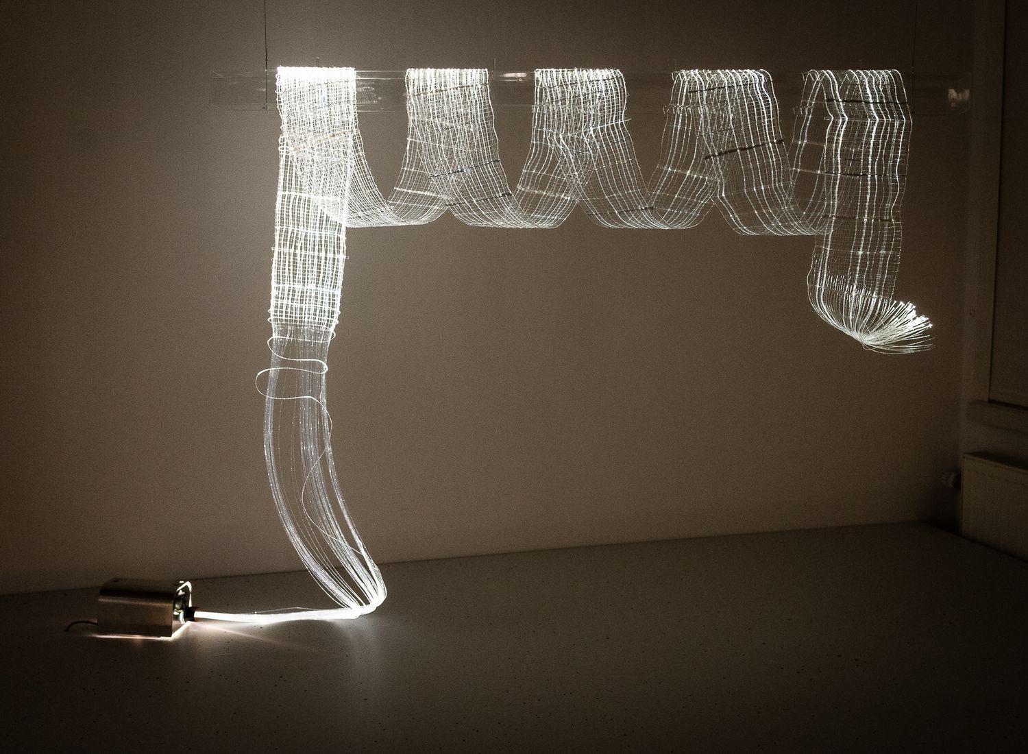 Illuminated fiber optic art installation creating glowing curved ribbon shapes against dark gallery wall.