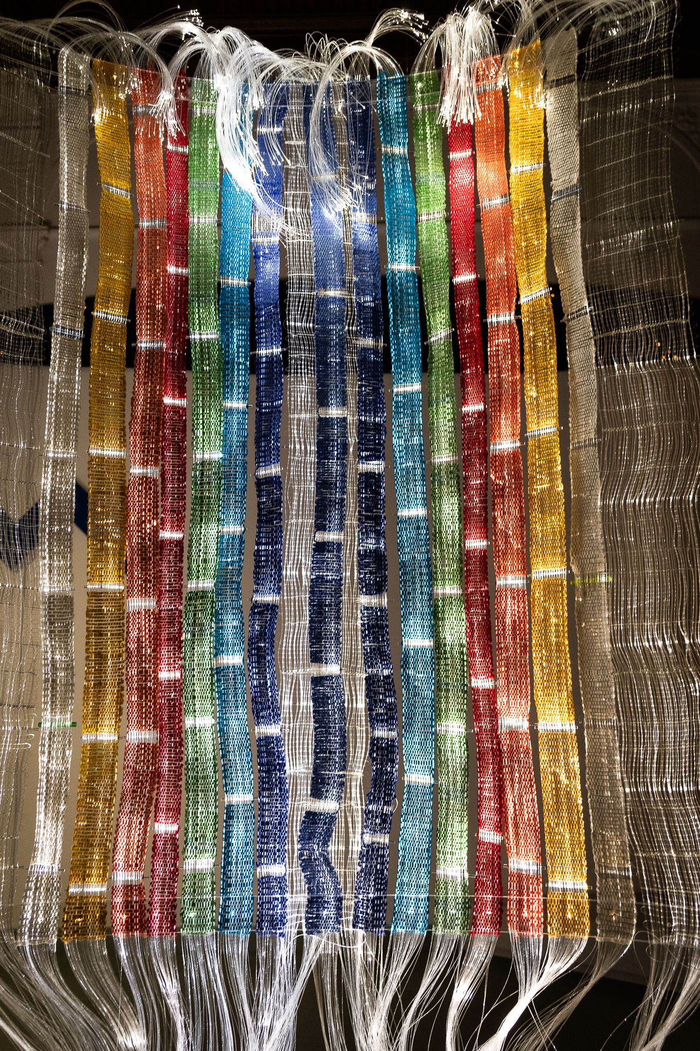 Colorful fiber optic strands woven into vertical panels displaying rainbow of colors including gold, red, blue and green.
