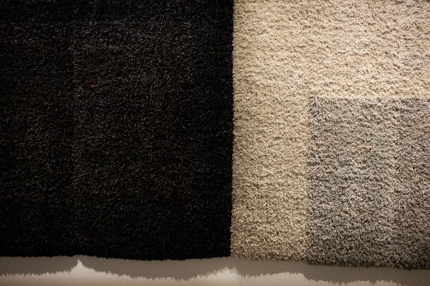 Close-up comparison of two carpet textures showing dark charcoal and light beige shag rug samples side by side.