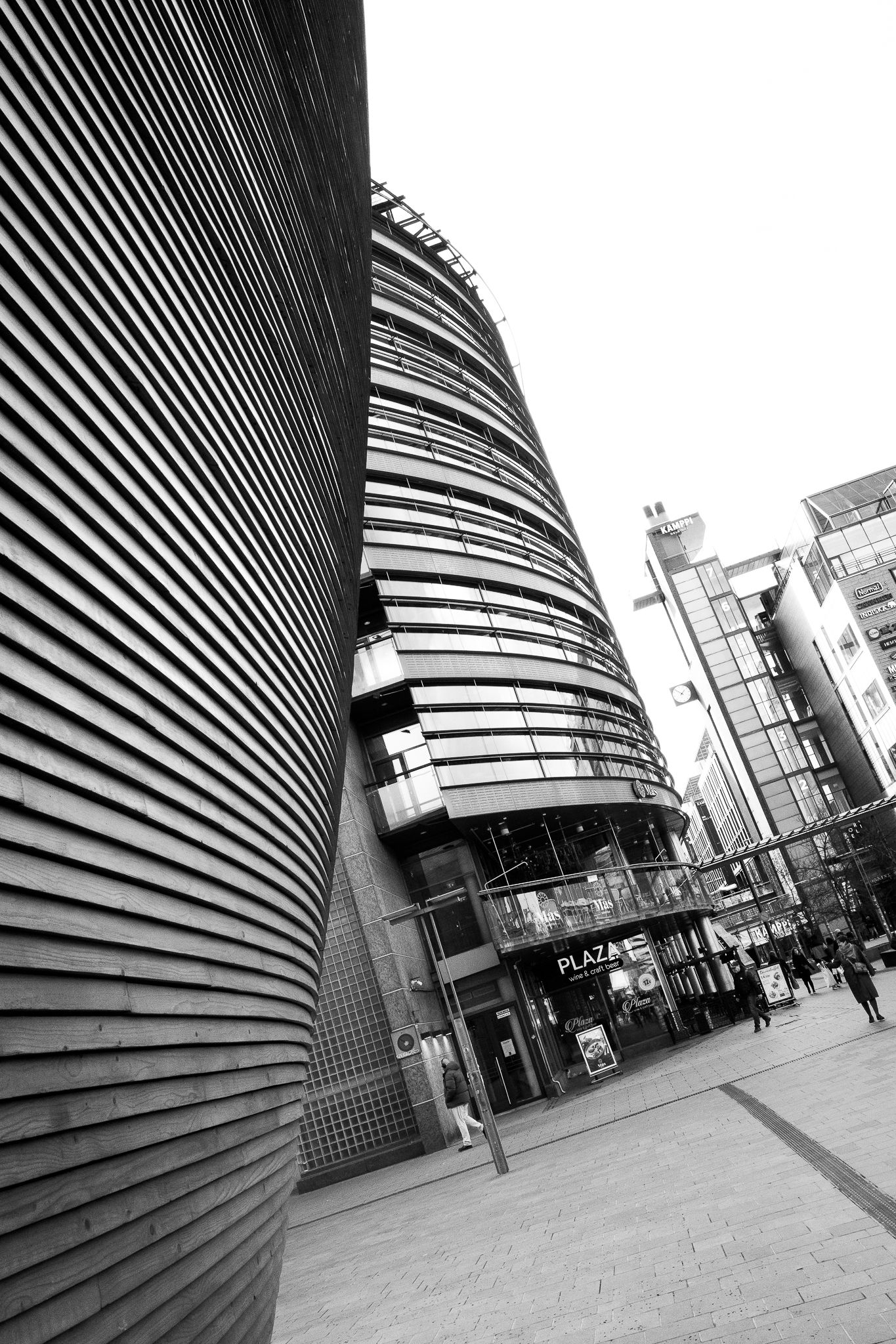 Black and white photo of modern curved building with horizontal metal louvers beside Plaza shopping center.