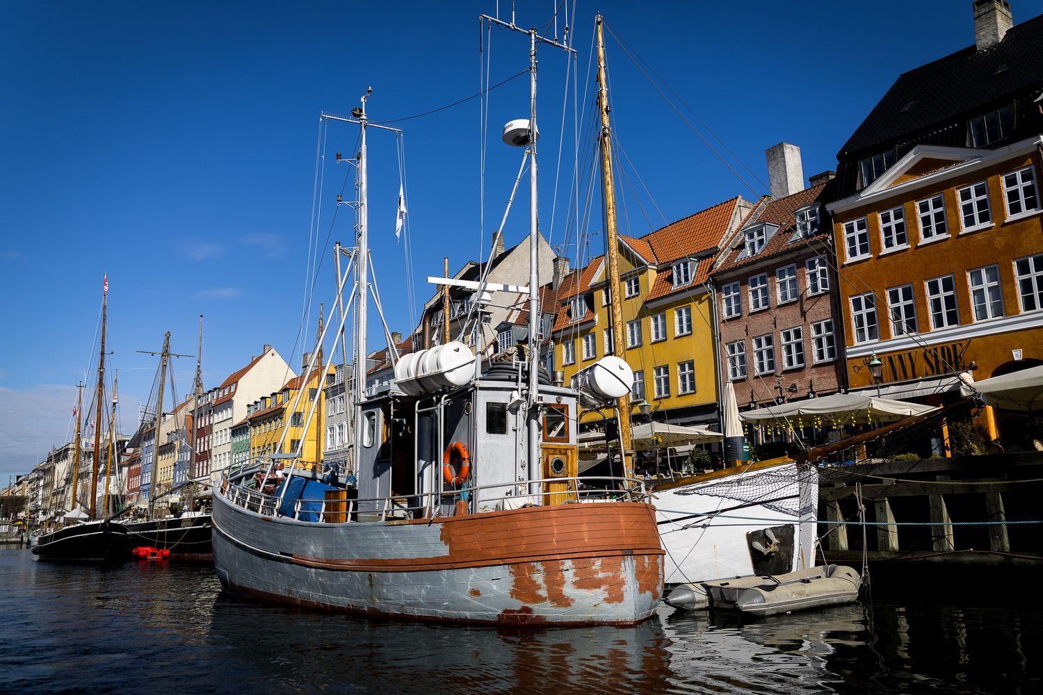 Weathered wooden sailboat moored at Nyhavn harbor with colorful Danish townhouses lining the waterfront.