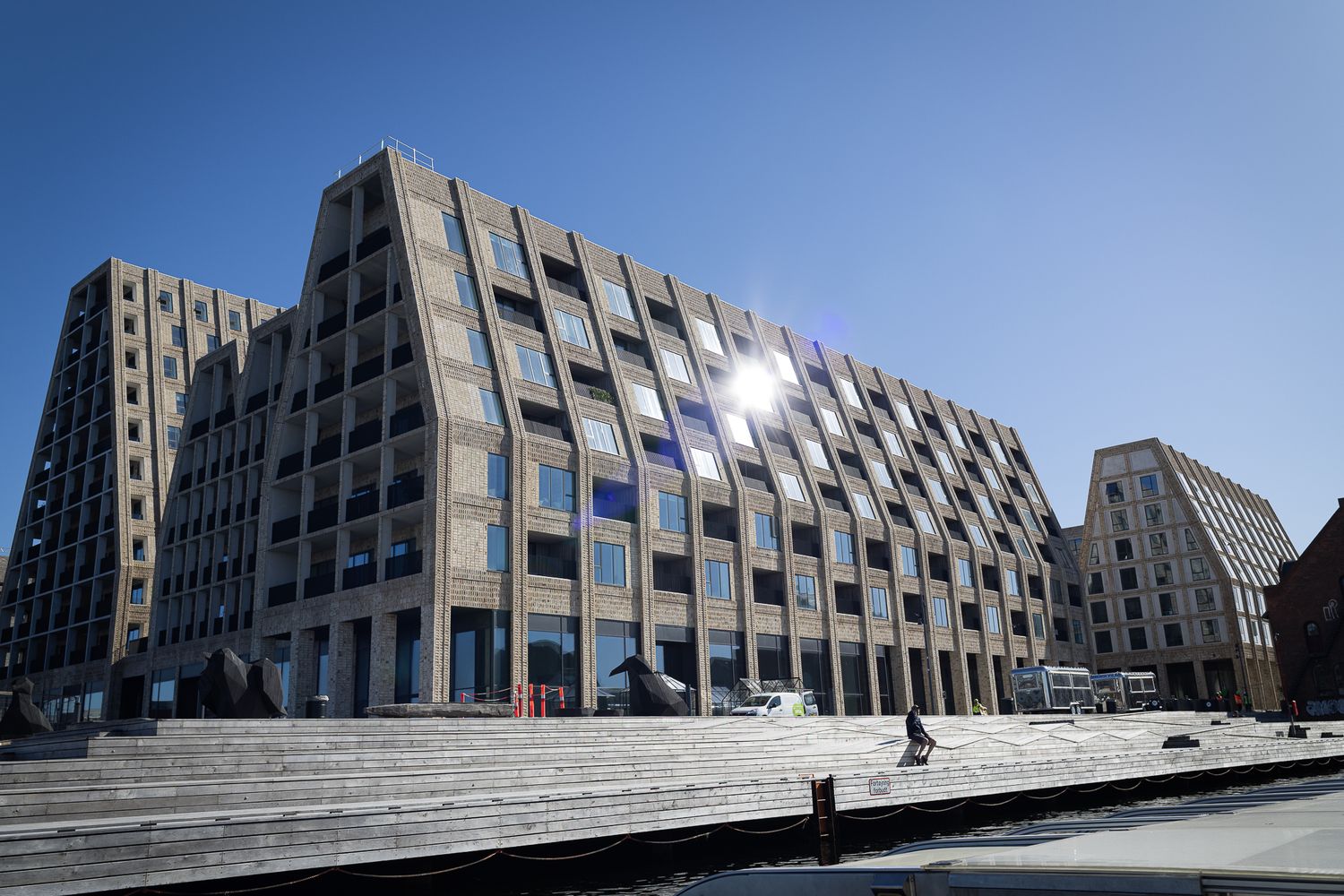 Contemporary geometric stone and glass residential building reflecting sunlight in Copenhagen's harbor district.