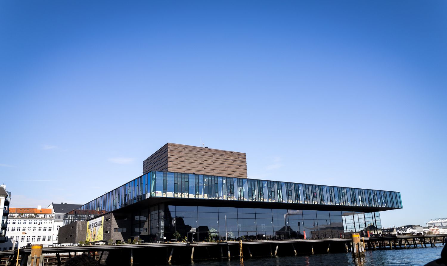 Copenhagen Royal Danish Playhouse modern glass theater building extending over the harbor waterfront on a sunny day.