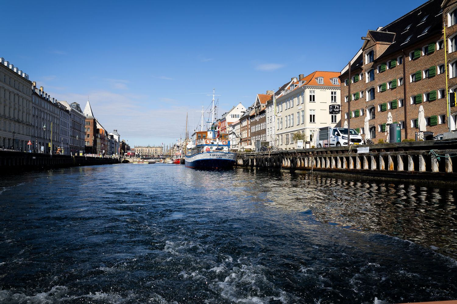 Scenic view down Nyhavn canal in Copenhagen with historic pastel buildings and moored boats on both sides.
