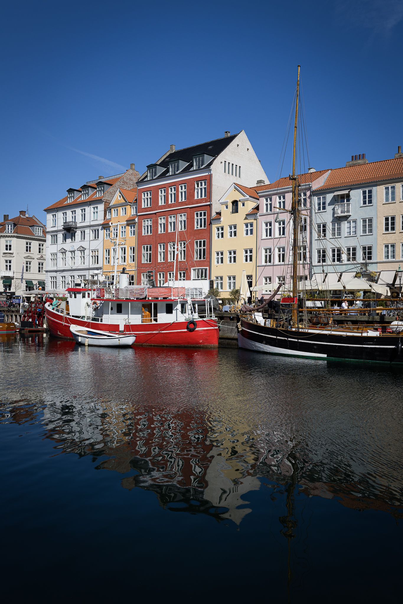 Colorful historic buildings reflected in the calm waters of Nyhavn canal in Copenhagen, Denmark.