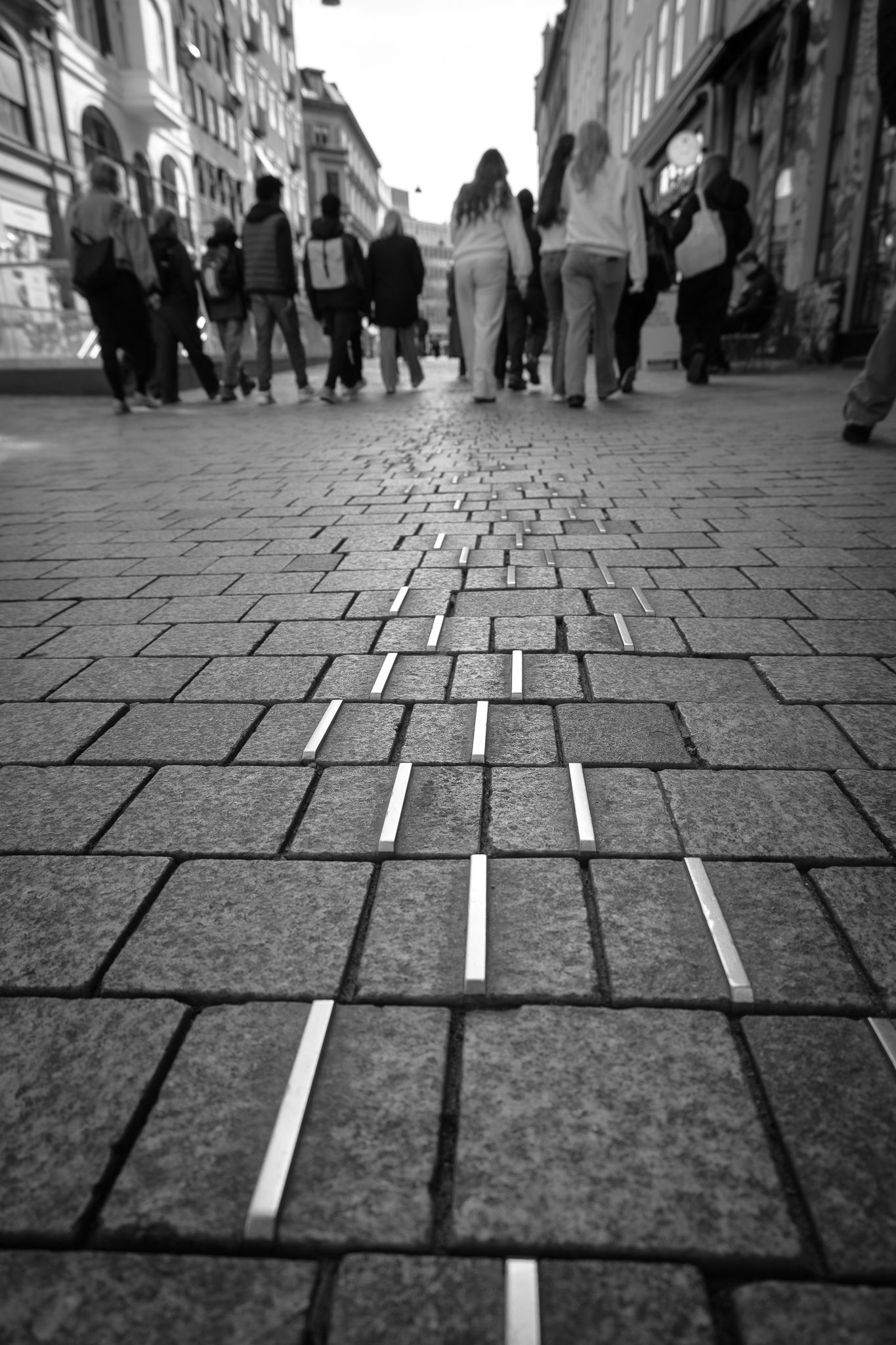 Black and white low angle view of cobblestone pedestrian street with people walking in city.