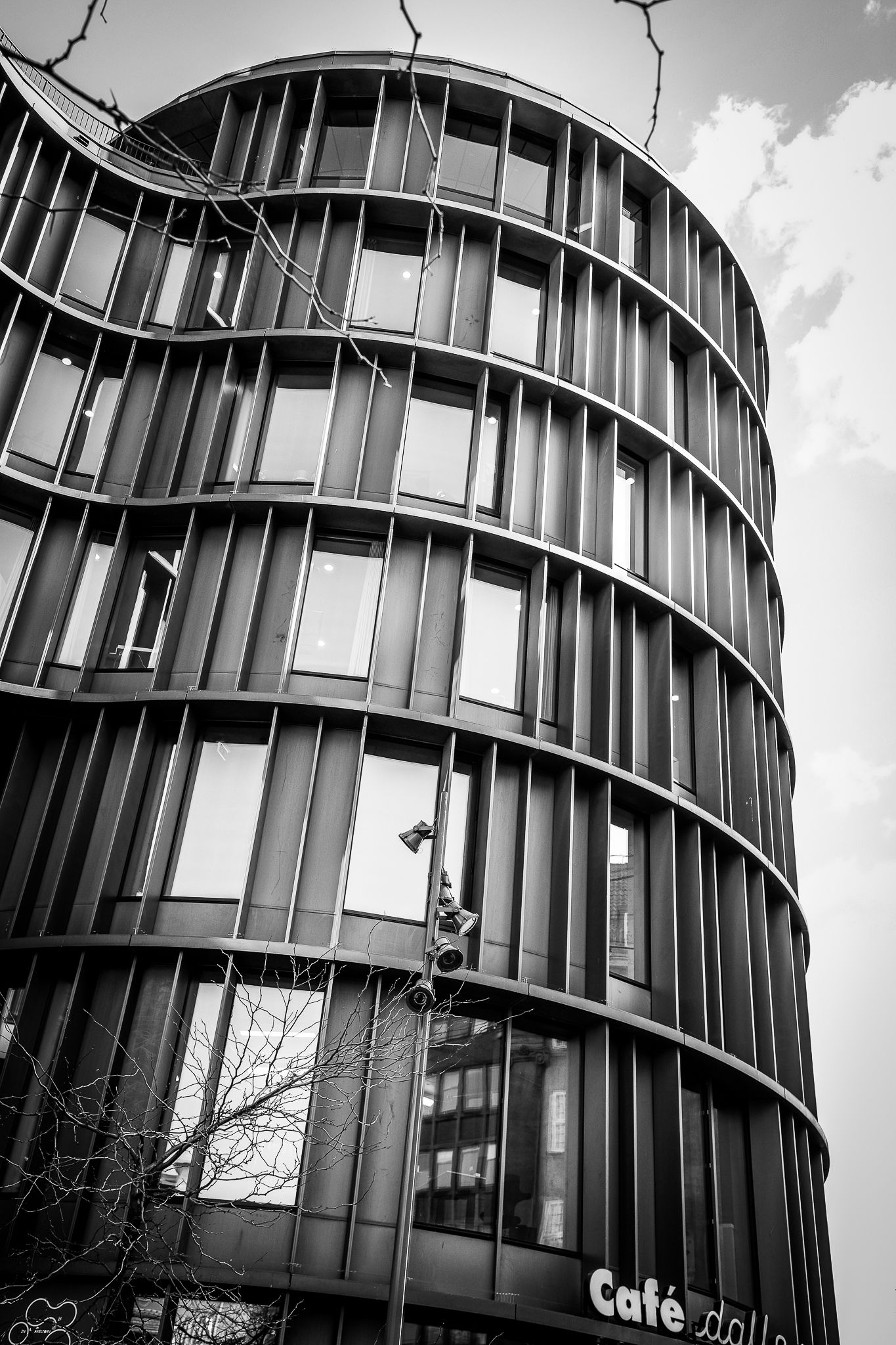 Black and white photo of curved modern building with vertical metal fins, Cafe sign visible below.
