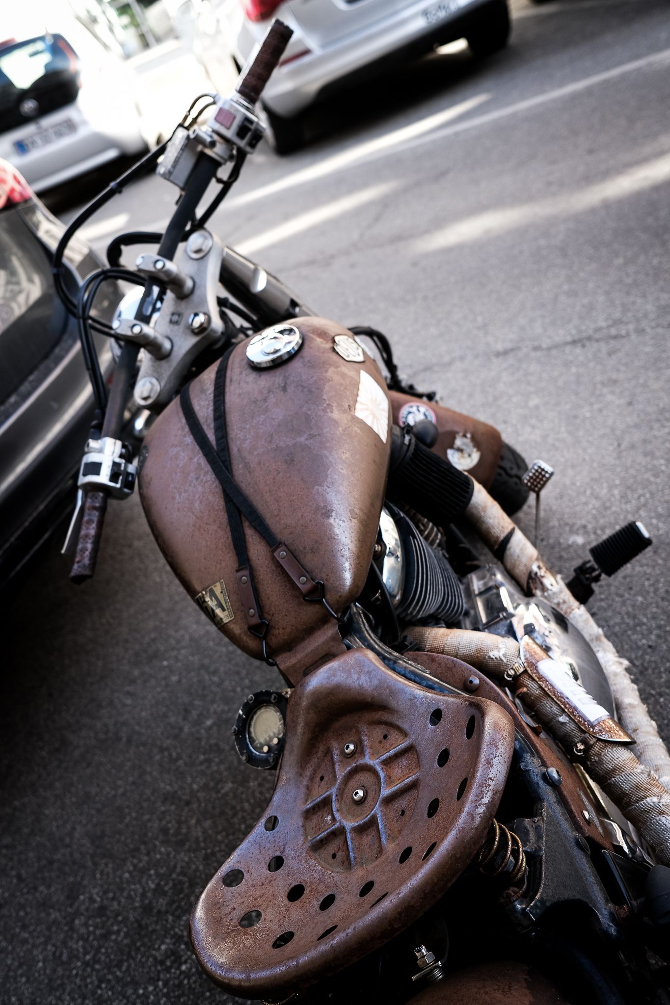 Vintage rusty custom bobber motorcycle with worn leather seat parked on city street.