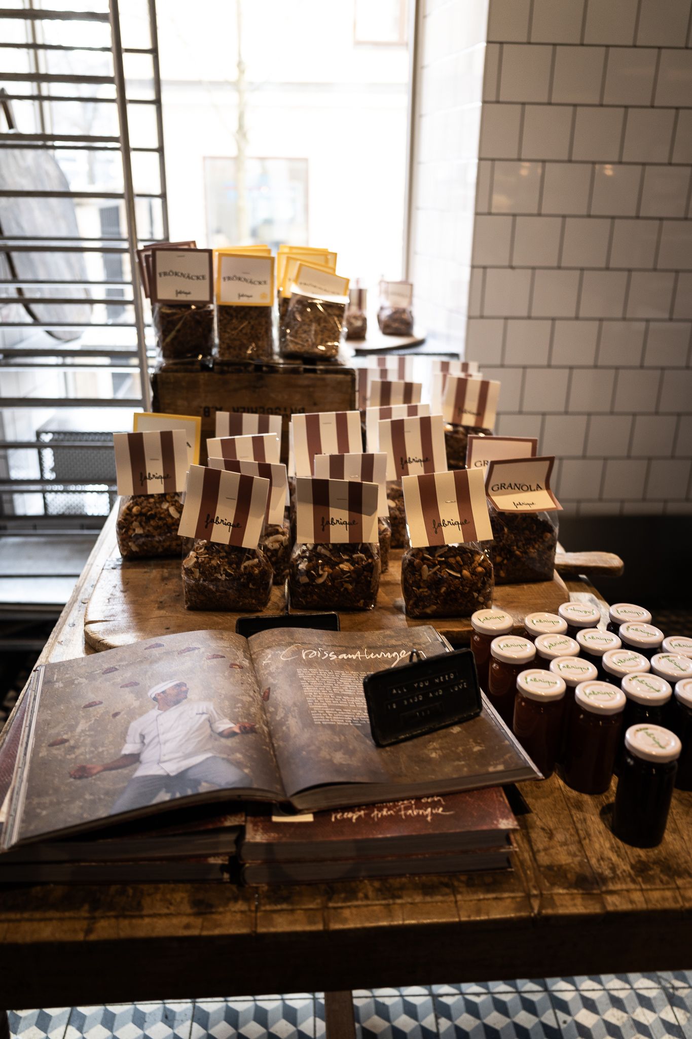Rustic wooden display table with striped packaged chocolates, jars of preserves and open cookbook in artisan shop.