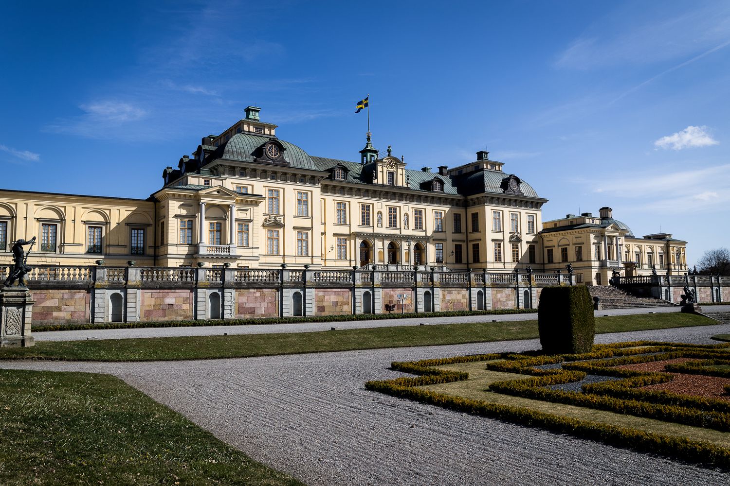 Drottningholm Palace facade with manicured gardens under blue sky in Stockholm, Sweden.