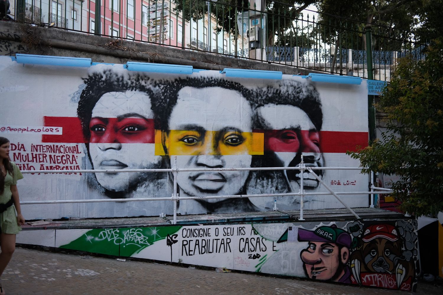 Colorful street art mural featuring three faces with red and yellow stripes on an urban wall.
