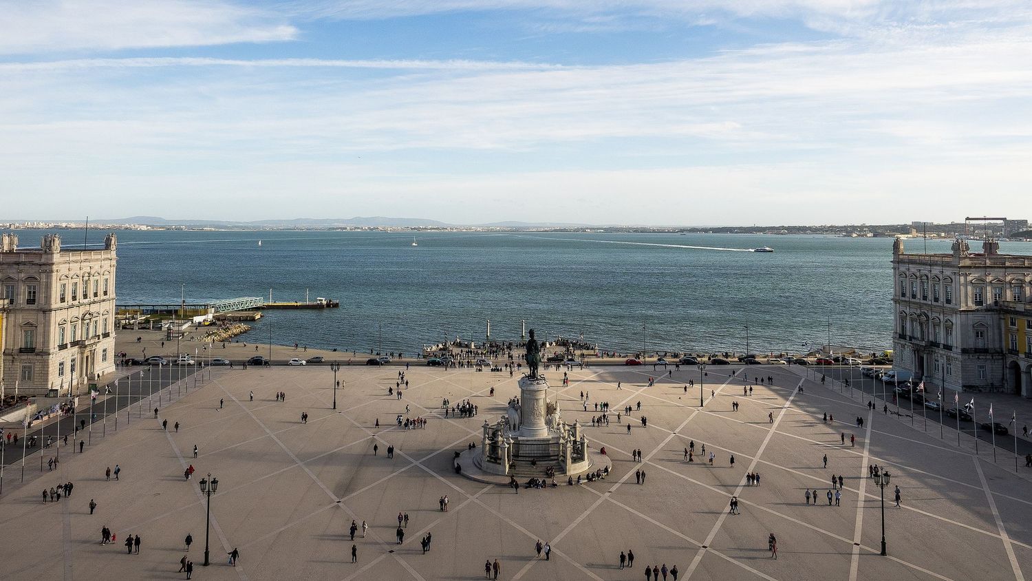 Aerial view of Praca do Comercio square in Lisbon with statue, cobblestones, and Tagus River backdrop.