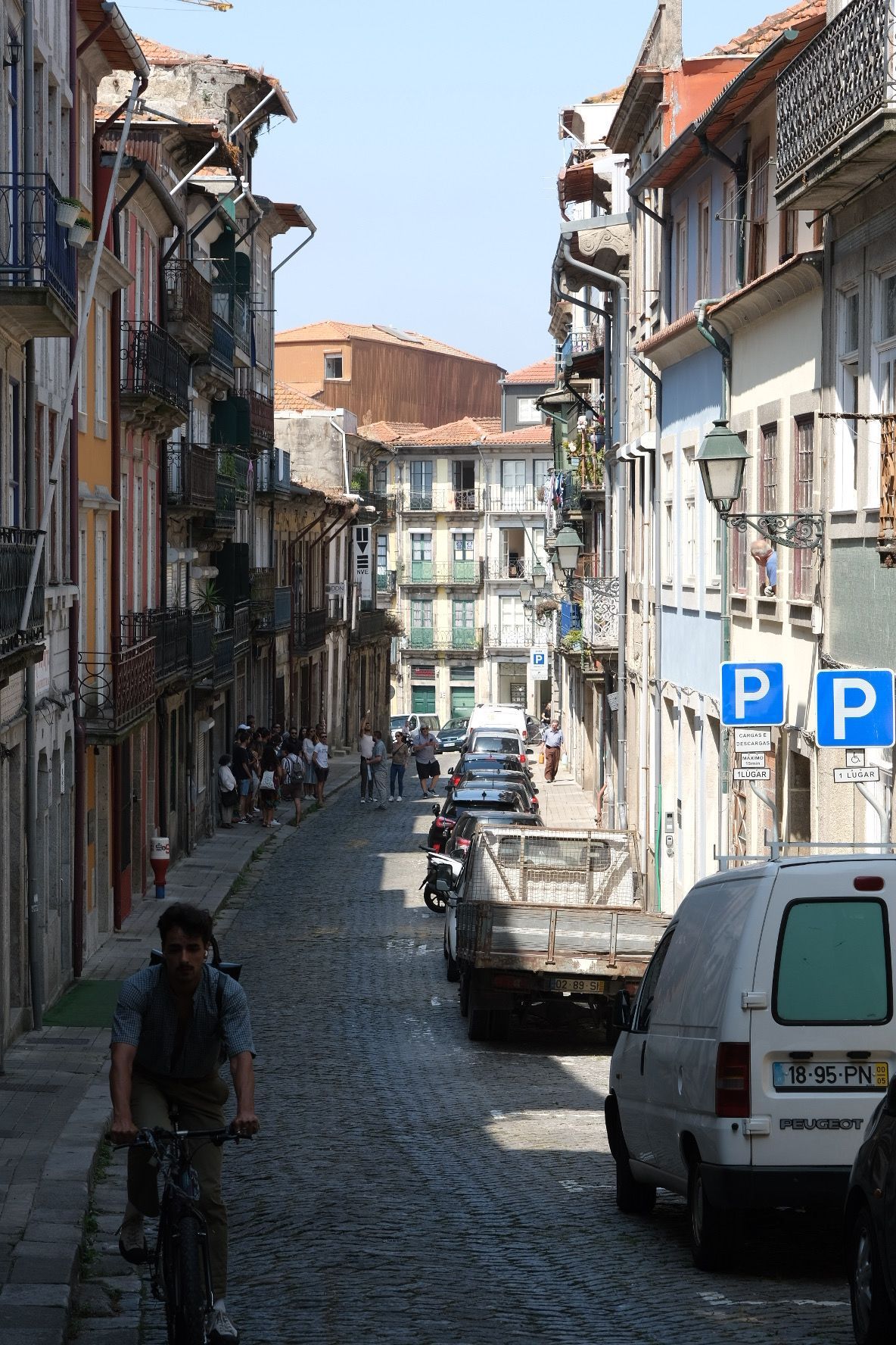 Narrow cobblestone street in Porto with colorful buildings, cyclists, and parked vehicles.