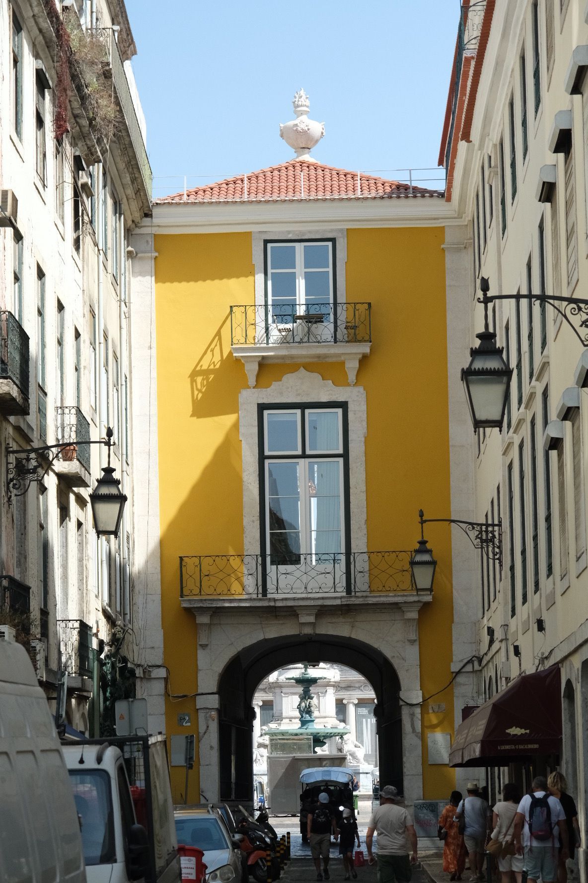 Bright yellow building with arch gateway on a narrow Lisbon street with street lamps.