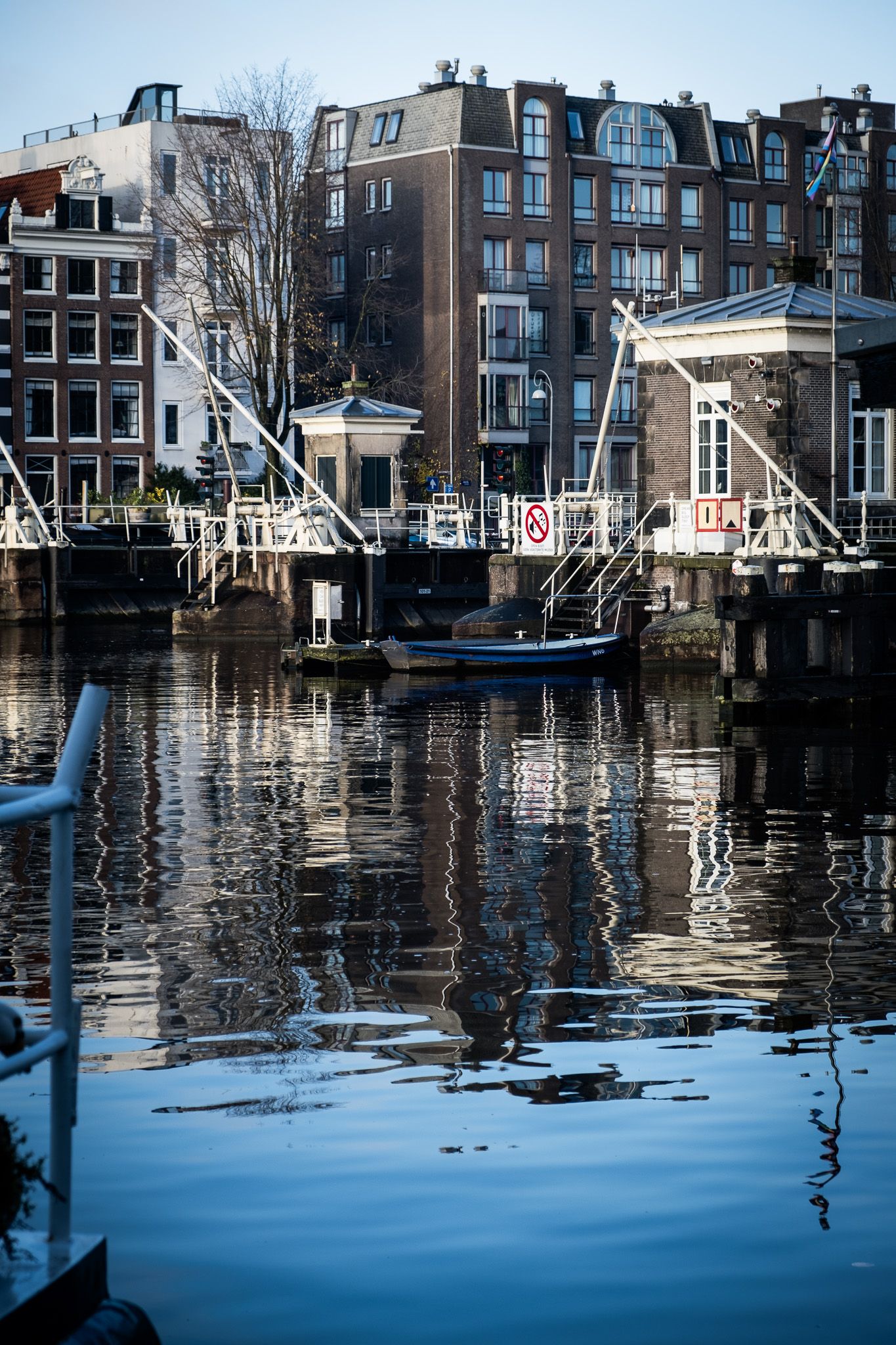 Calm Amsterdam canal reflecting historic brick buildings and a drawbridge on a sunny day.