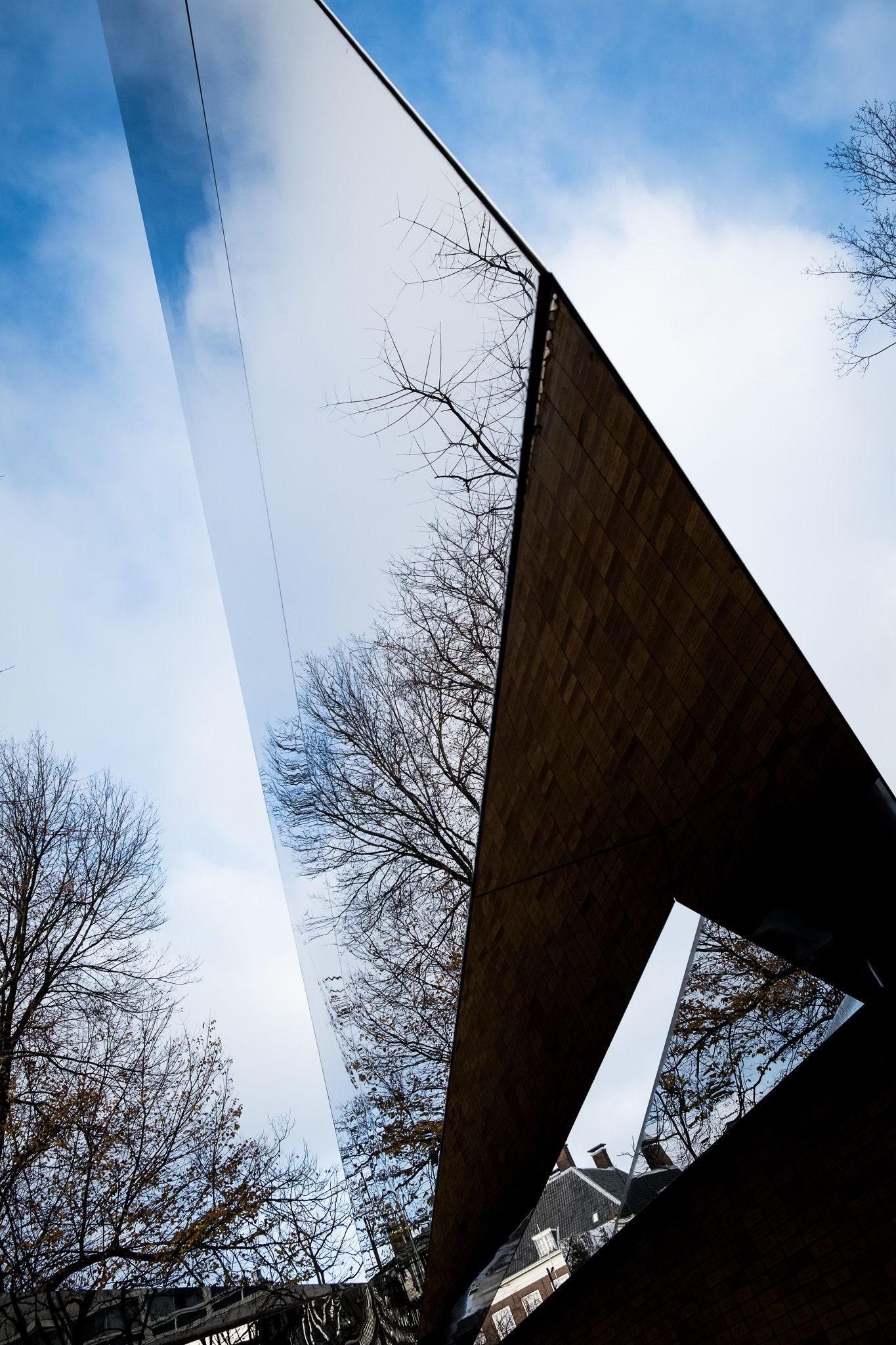 Low-angle view of a modern mirrored architectural sculpture against a blue cloudy sky.