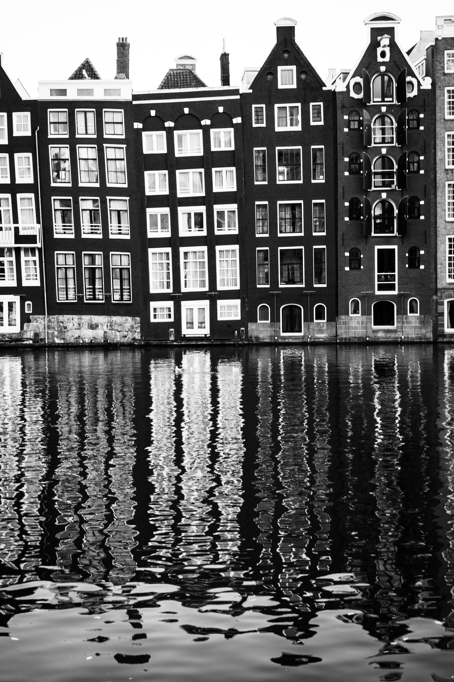 Black and white photo of classic Amsterdam canal houses reflecting in still water.